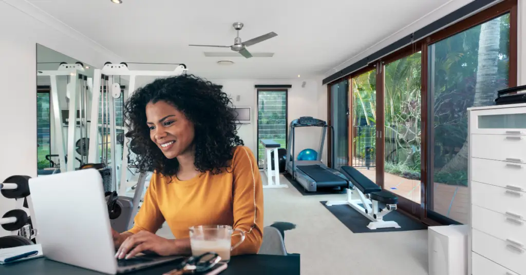 Should you have a home gym if you work from home? Woman at a desk with a home gym behind her